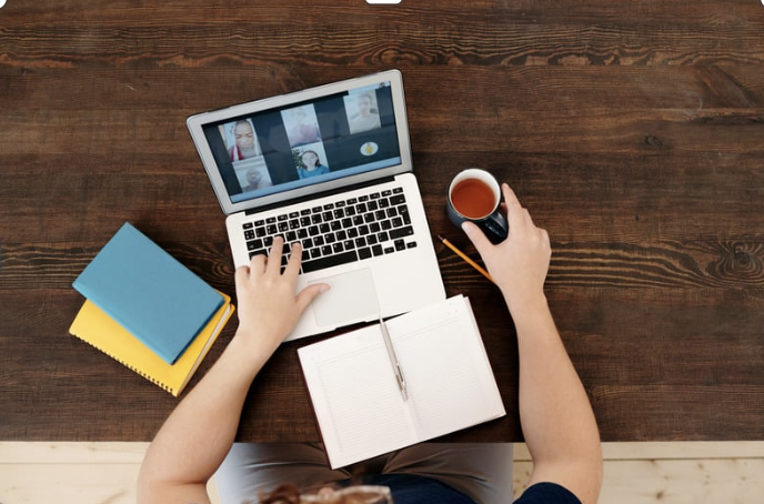 Birds-eye view photo of a person sitting at desk with their laptop and a cup of tea. The person is logged onto a video conference.
